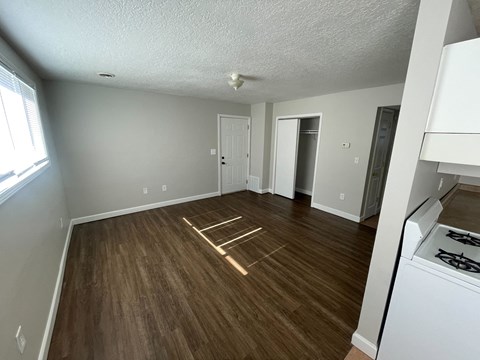 an empty living room with wood flooring and a kitchen